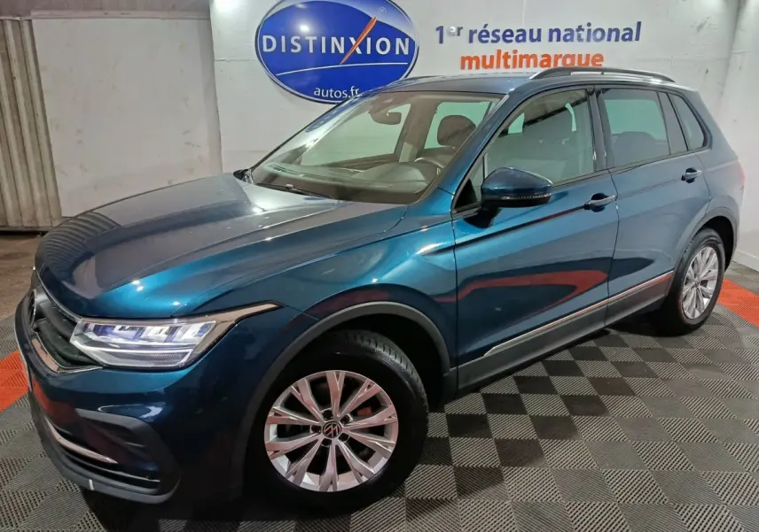 Volkswagen Tiguan bleu en 3/4 avant droit, avec jantes alliage et phares LED visibles en intérieur showroom.