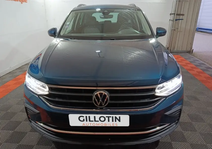 Vue avant frontale du Volkswagen Tiguan bleu avec phares LED allumés dans un showroom intérieur.