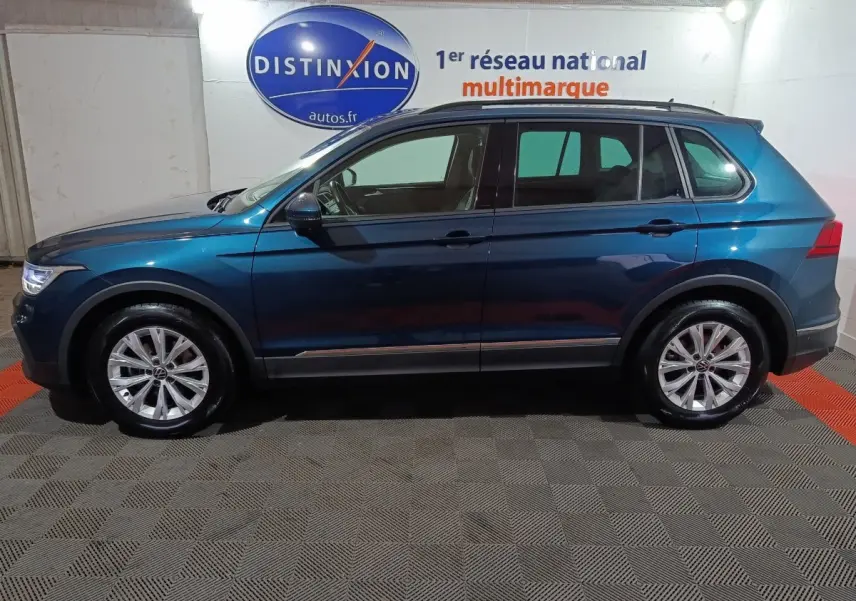 Vue latérale droite d'un Volkswagen Tiguan bleu 2021 garé en intérieur avec jantes alliage et toit noir.