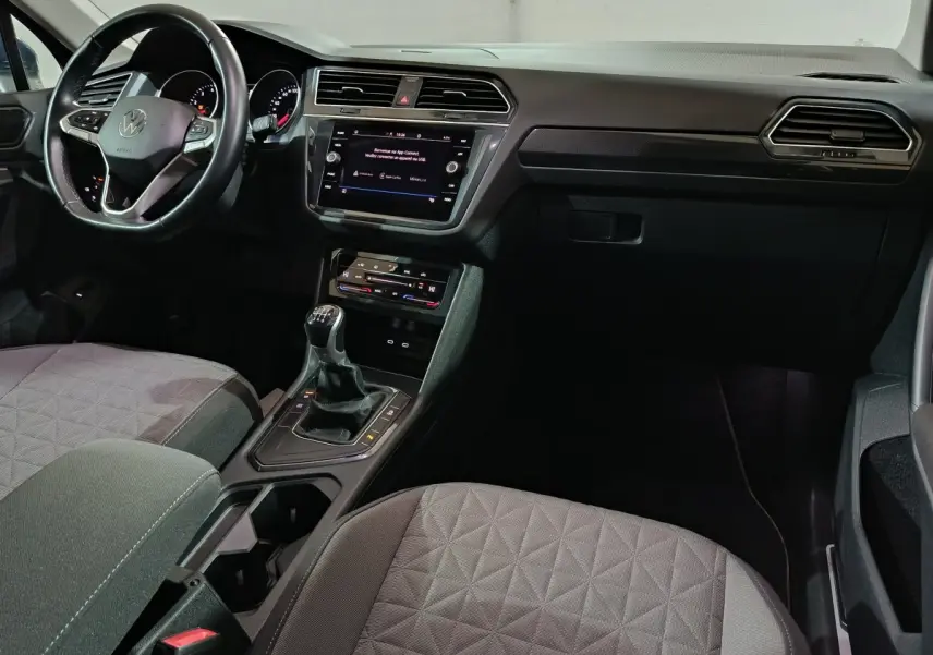 Vue intérieure côté conducteur du Volkswagen Tiguan 2021 avec volant cuir, tableau de bord noir et levier de vitesses manuel.