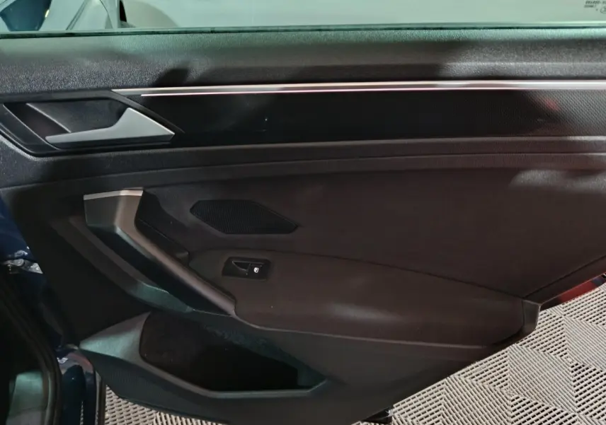 Vue intérieure côté gauche de la porte avant d’un Volkswagen Tiguan bleu, avec poignée et commande de vitre électrique.