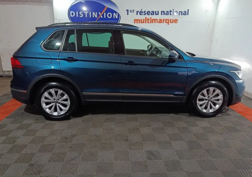 Vue de profil côté gauche d’un Volkswagen Tiguan bleu 2021 garé en intérieur sur sol carrelé.