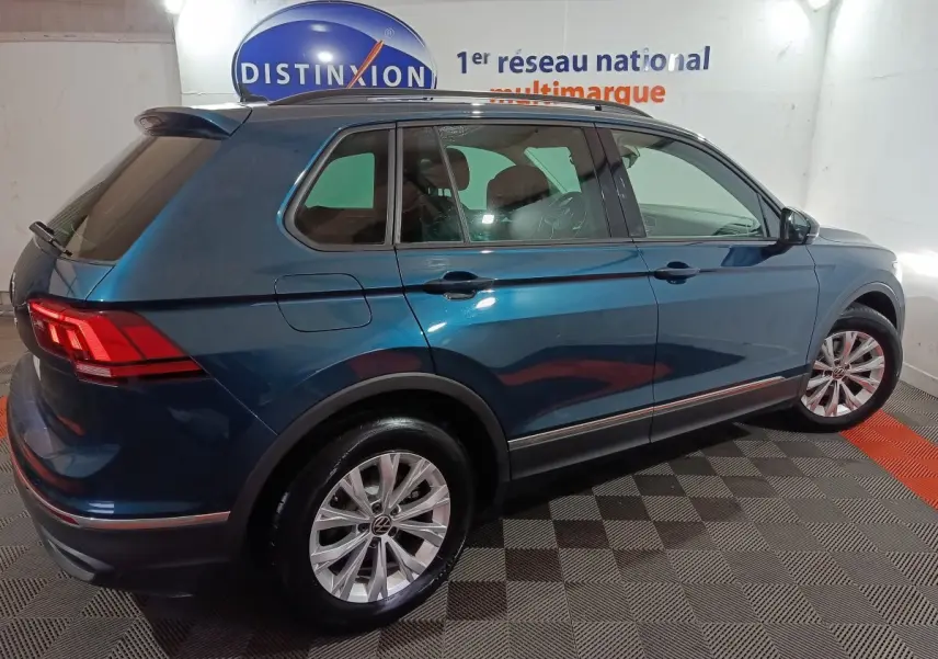 Vue 3/4 arrière droite d'un Volkswagen Tiguan bleu 2021 dans un showroom avec éclairage intérieur.
