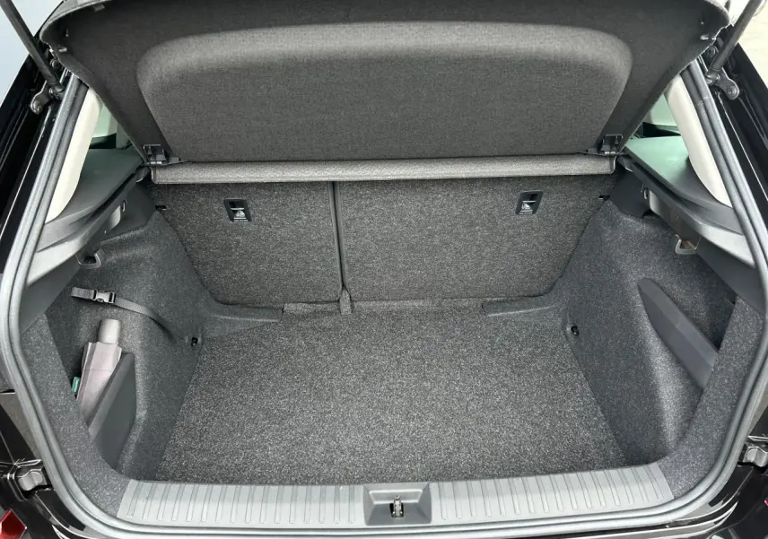 Coffre ouvert vu de l'arrière d'un Skoda Kamiq noir Magic, intérieur gris et compartiments latéraux visibles.