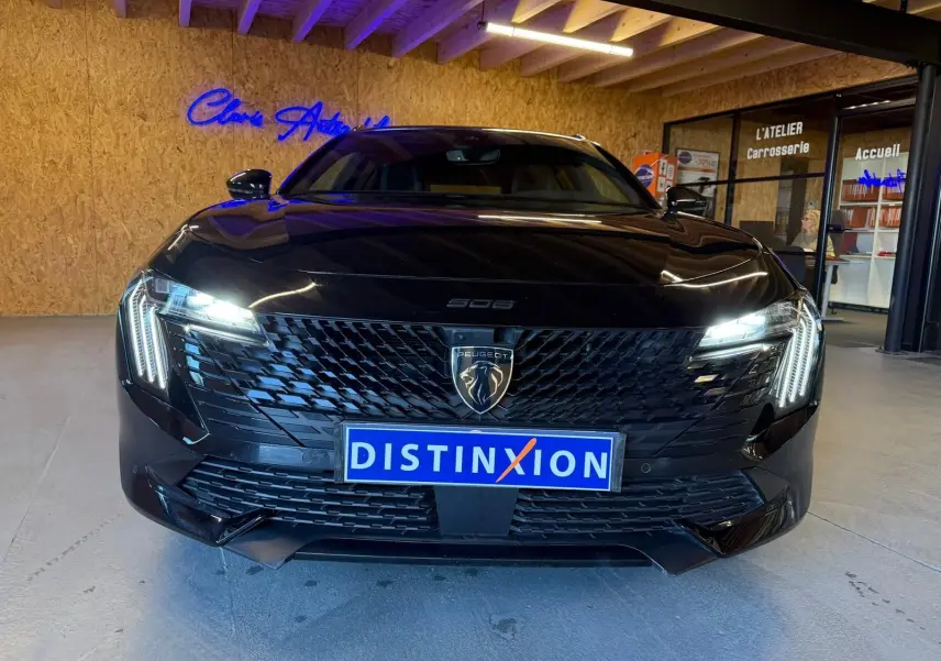 Vue frontale d'une Peugeot 508 SW noire avec calandre noire brillante et feux LED allumés en intérieur showroom.