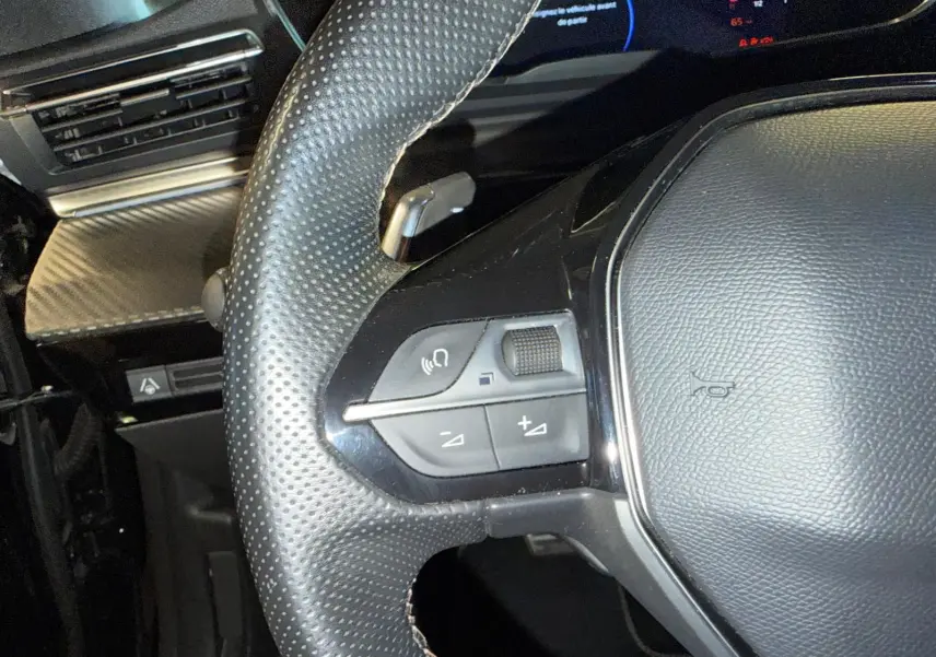 Gros plan sur le volant cuir perforé noir du Peugeot 508 SW 2024 avec commandes intégrées et décor carbone en arrière-plan.