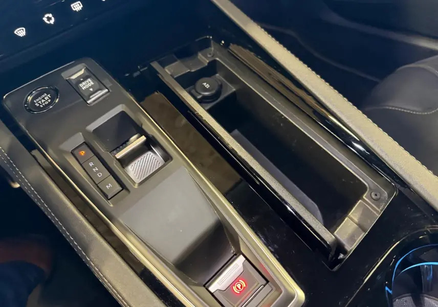 Gros plan sur la console centrale noire brillante de la Peugeot 508 SW 2024 avec sélecteur de boîte auto et frein électrique.