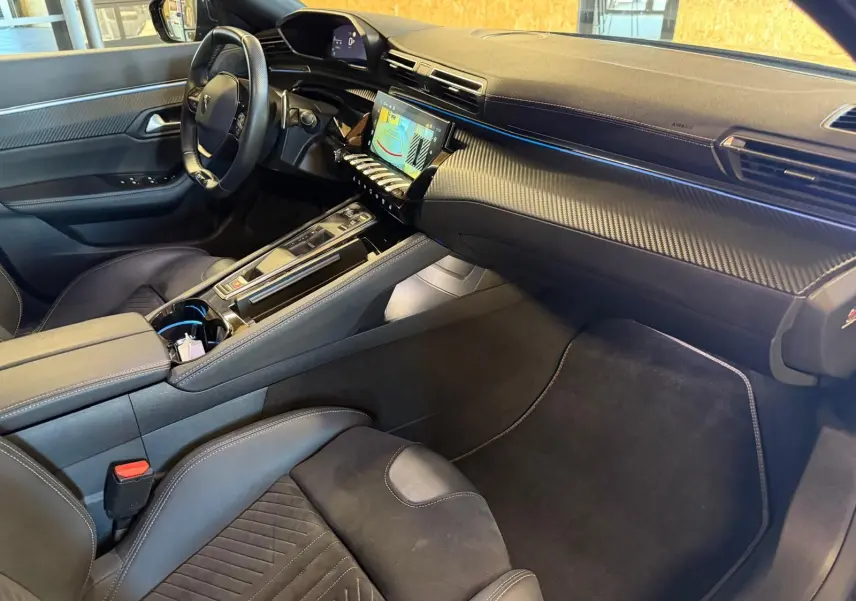 Vue intérieure côté passager du Peugeot 508 SW 2024 noir, avec tableau de bord carbone et éclairage d'ambiance bleu.