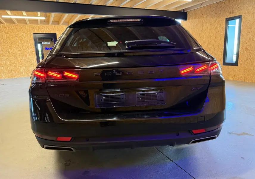 Vue arrière d’un break Peugeot 508 SW noir avec feux LED allumés et badges PEUGEOT et GT visibles.