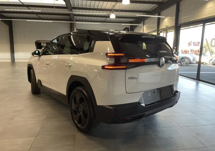 Vue 3/4 arrière droite du Citroën C5 Aircross blanc Okenite avec toit noir et feux arrière LED allumés en intérieur showroom.