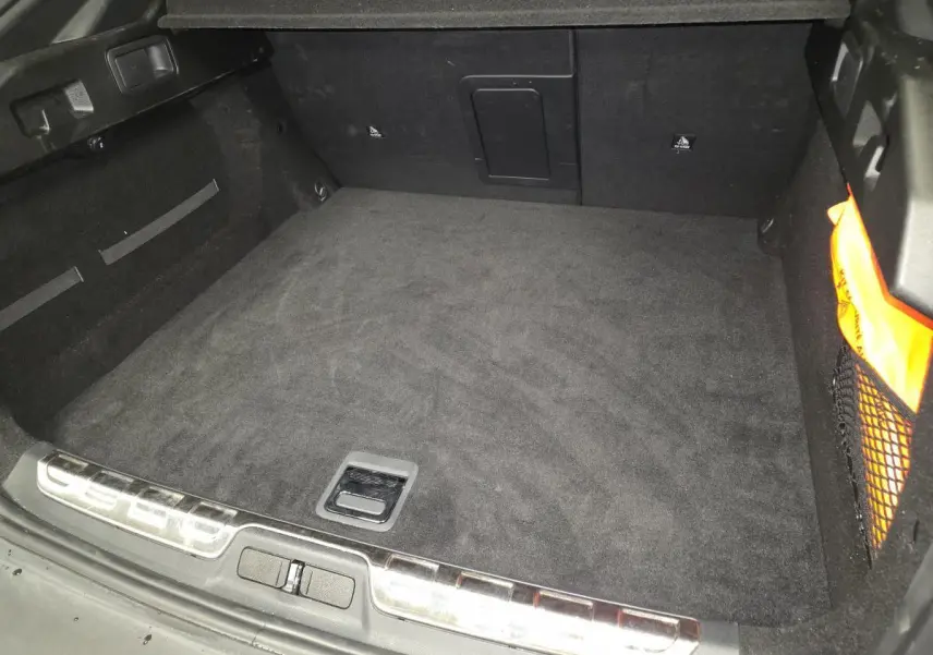 Coffre vide vu de l'arrière d'une Peugeot 408 1.6 PHEV 2024, intérieur noir avec filet de rangement latéral.