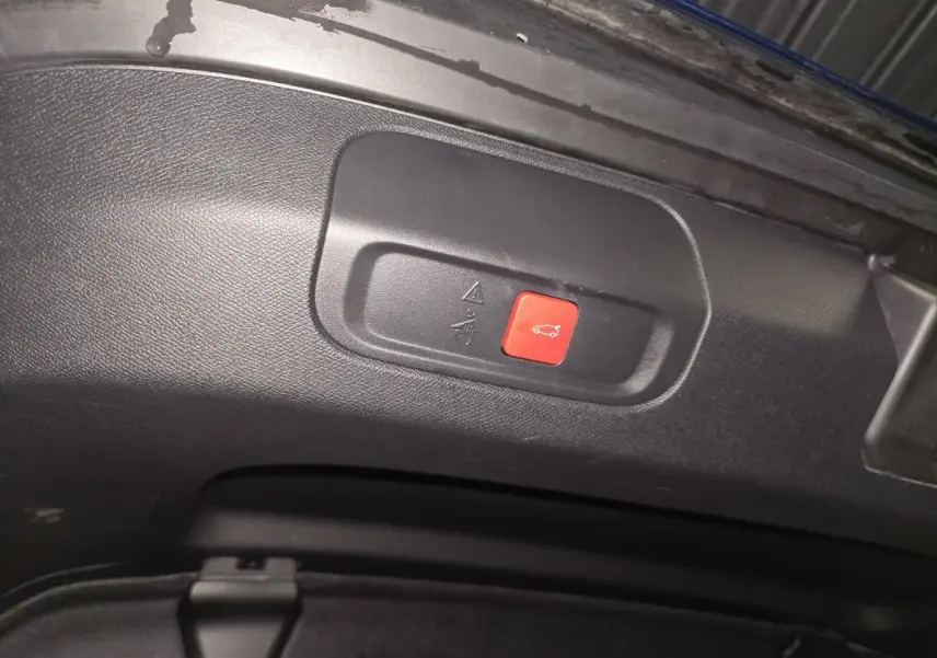 Bouton rouge d'ouverture électrique du hayon sur la partie intérieure du coffre d'une Peugeot 408 bleu.