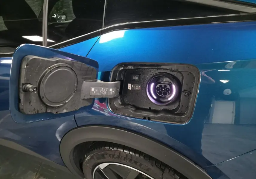 Prise de recharge ouverte côté gauche sur la carrosserie bleu métallisé du Peugeot 408 hybride rechargeable.