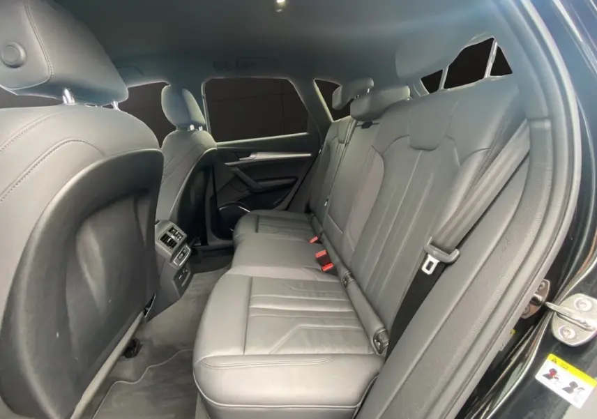 Vue intérieure côté droit sur la banquette arrière en cuir gris du SUV Audi Q5 noir, avec accoudoir central et ceintures visibles.