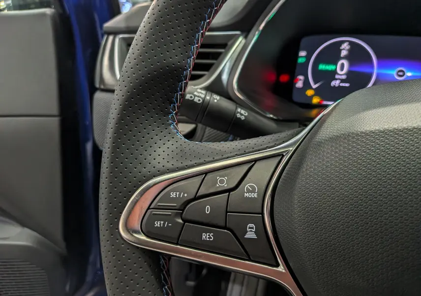 Gros plan sur le volant perforé noir avec surpiqûres bleues du Renault Captur E-Tech, tableau de bord digital en arrière-plan.