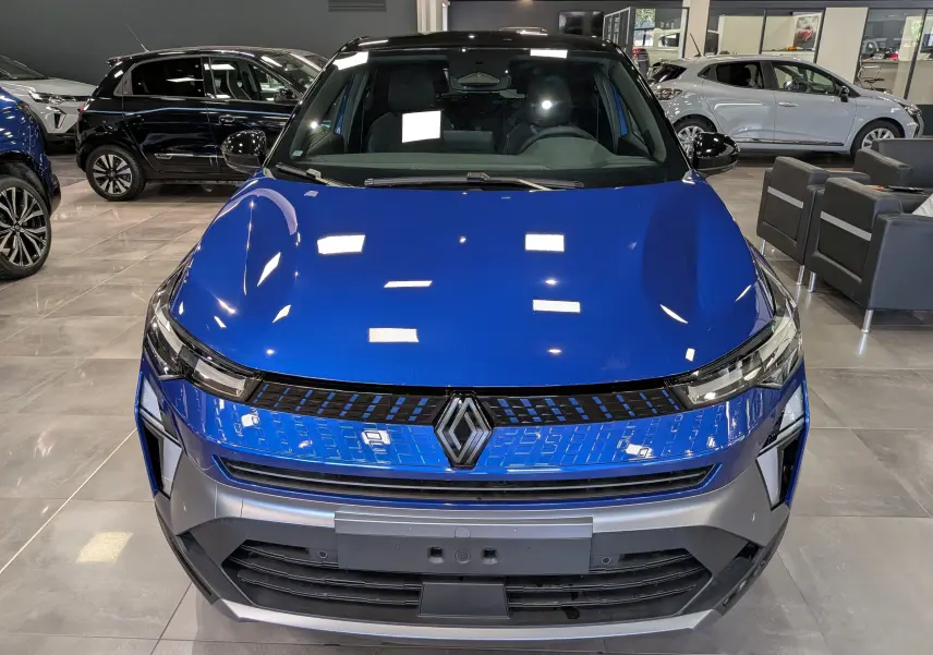 Vue avant d'un Renault Captur E-TECH hybride 2026 bleu Iron avec toit noir, dans un showroom lumineux.