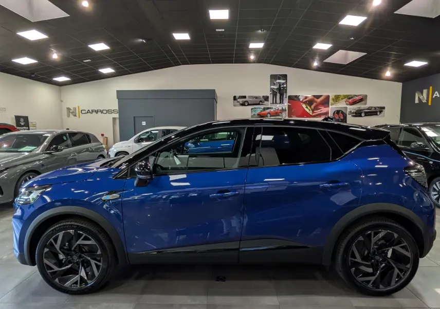Profil côté gauche du Renault Captur E-TECH hybride bleu Iron avec toit noir, jantes noires et intérieur visible en showroom.