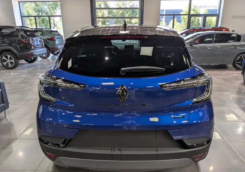 Vue arrière d’un Renault Captur E-TECH hybride bleu Iron avec toit noir, dans un showroom lumineux.