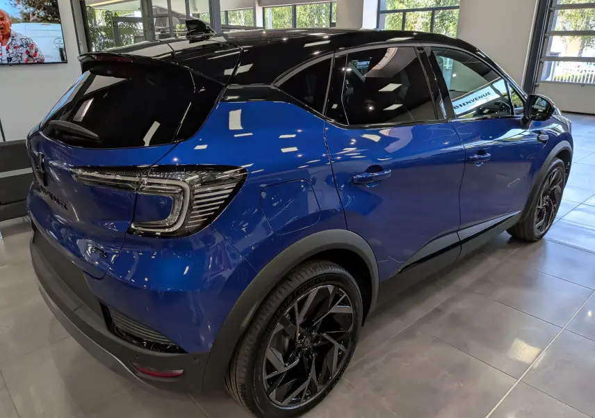 Vue 3/4 arrière droite d’un Renault Captur E-TECH hybride bleu Iron avec toit noir et jantes noires en showroom.