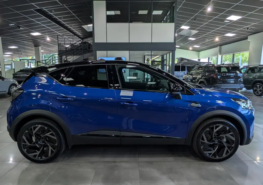 Profil côté gauche du Renault Captur E-TECH hybride 2026 en Bleu Iron avec toit noir et jantes noires en showroom.