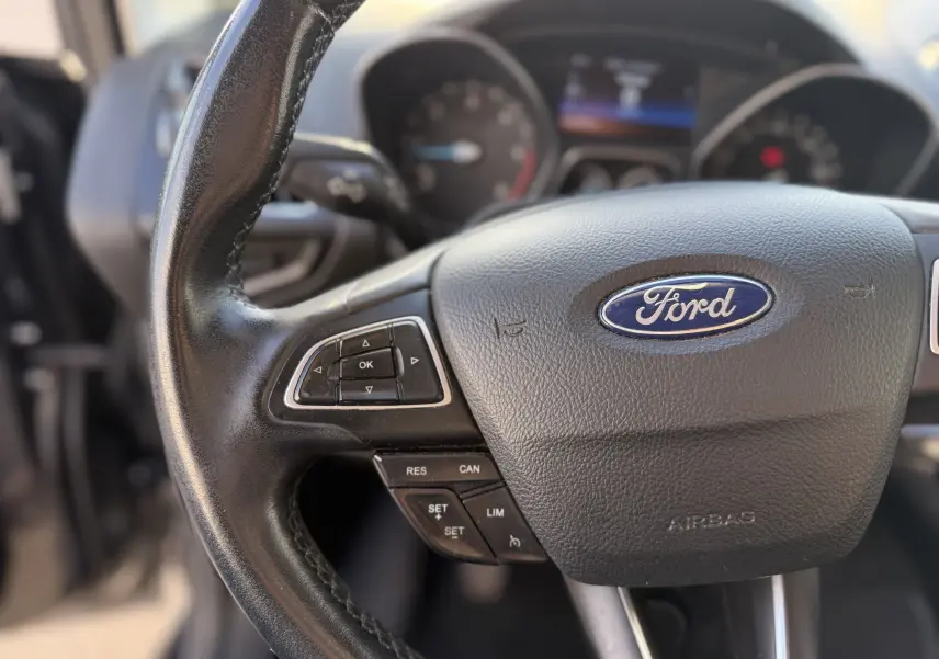Gros plan sur le volant en cuir noir d’une Ford C-MAX 2018, avec commandes intégrées et logo Ford central visible.