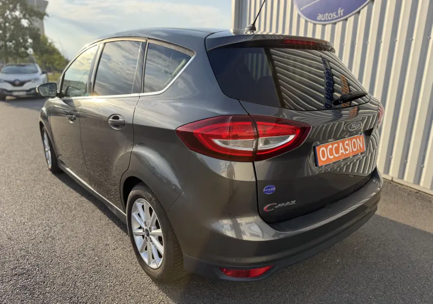 Vue 3/4 arrière droite d'une Ford C-MAX gris foncé avec vitres teintées et plaque "OCCASION" sur un parking extérieur.