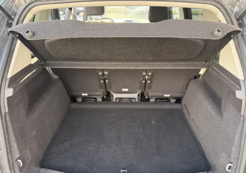 Coffre ouvert de la Ford C-MAX 1.6 TDCI 120 Titanium, vue arrière montrant l'espace de chargement vide et la tablette cache-bagages relevée.