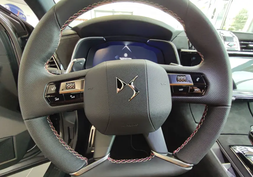 Vue rapprochée du volant perforé gris du DS7 Crossback E-TENSE 2022 avec commandes intégrées et coutures rouges contrastantes.