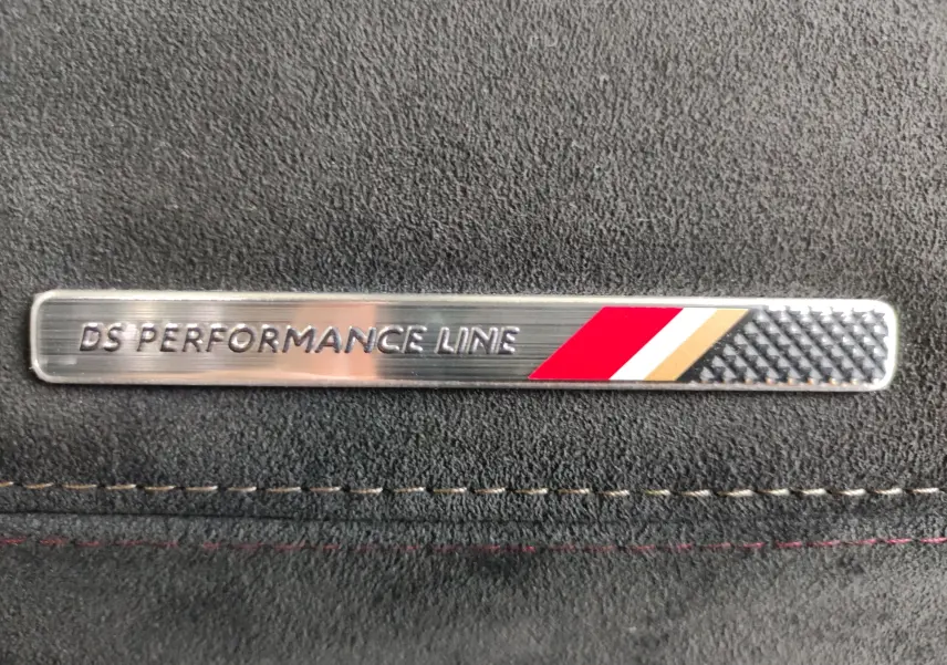 Gros plan sur l’inscription DS Performance Line sur une plaque métallique intégrée dans un revêtement noir intérieur.