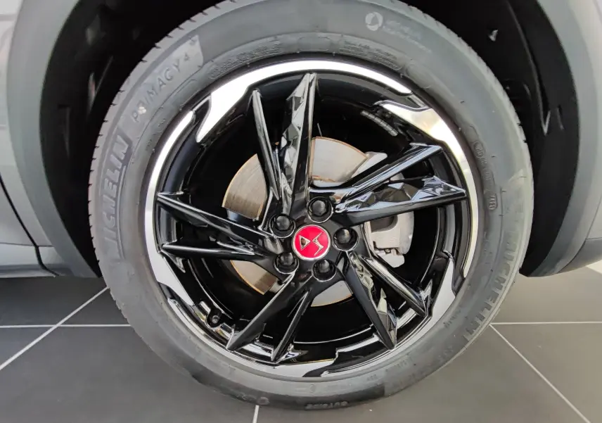 Gros plan sur la jante noire brillante avec logo DS rouge du DS7 Crossback E-TENSE gris, roue avant droite visible.