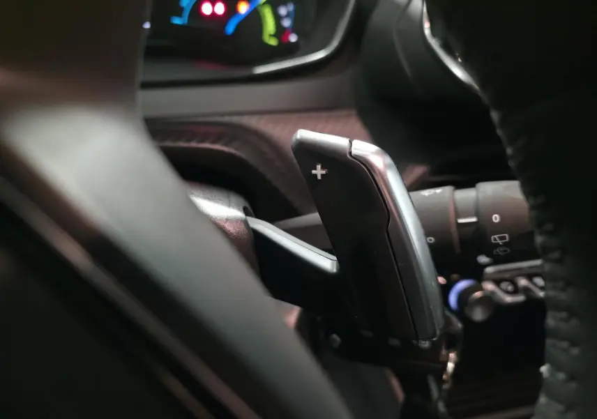 Gros plan sur la palette de changement de vitesse "+" derrière le volant du Peugeot 2008 gris, intérieur sombre.