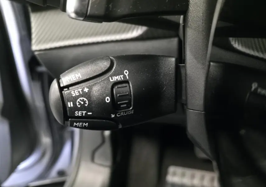 Gros plan sur la commande de régulateur de vitesse noire dans l'habitacle du Peugeot 2008 gris 2025.