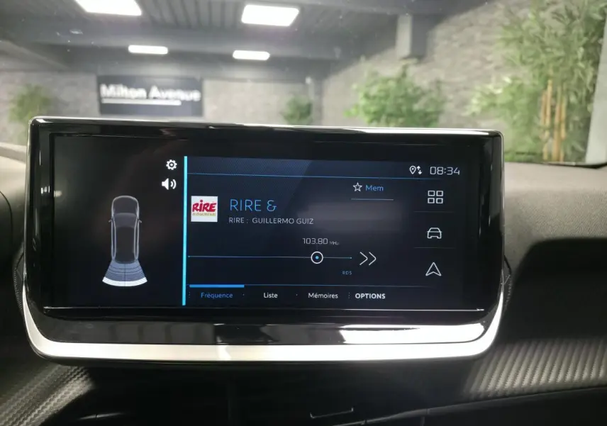 Écran tactile central du Peugeot 2008 2025 affichant la radio, avec tableau de bord et décor carbone visibles.