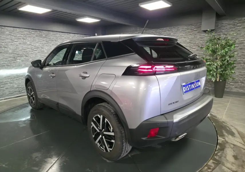 Peugeot 2008 gris métallisé vue 3/4 arrière droit, feux LED allumés et jantes noires avec inserts argentés.