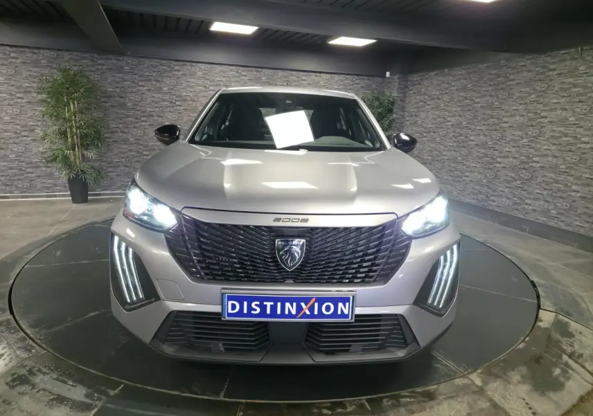 Vue de face du Peugeot 2008 gris avec calandre noire et feux LED allumés dans un showroom.