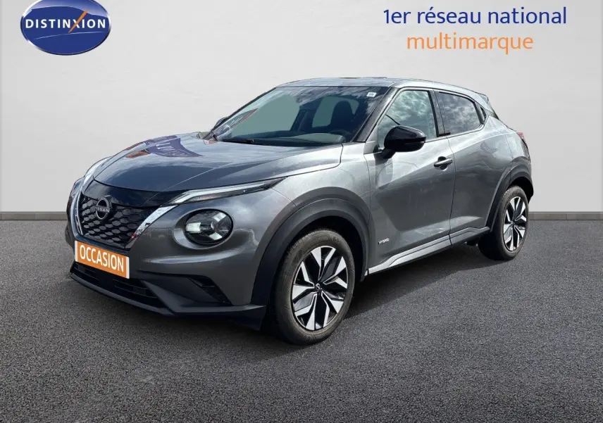 Nissan Juke Hybrid gris squale métal en 3/4 avant droit, avec jantes distinctives et calandre noire brillante.