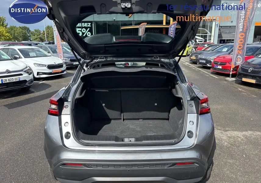 Vue arrière du Nissan Juke Hybrid gris squale métal 2024 avec coffre ouvert, montrant l’espace de chargement vide.