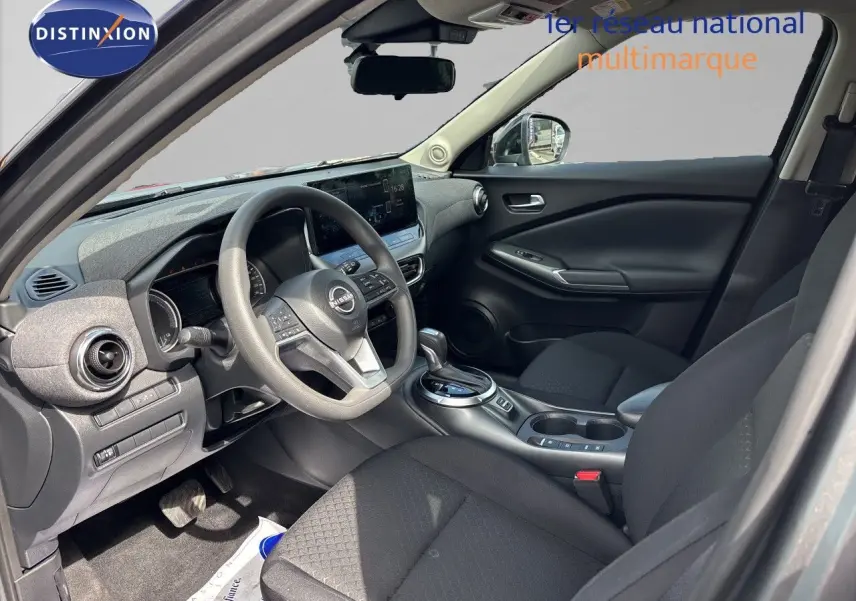 Vue intérieure côté conducteur du Nissan Juke Hybrid 2024 avec tableau de bord gris et sièges tissu noir.