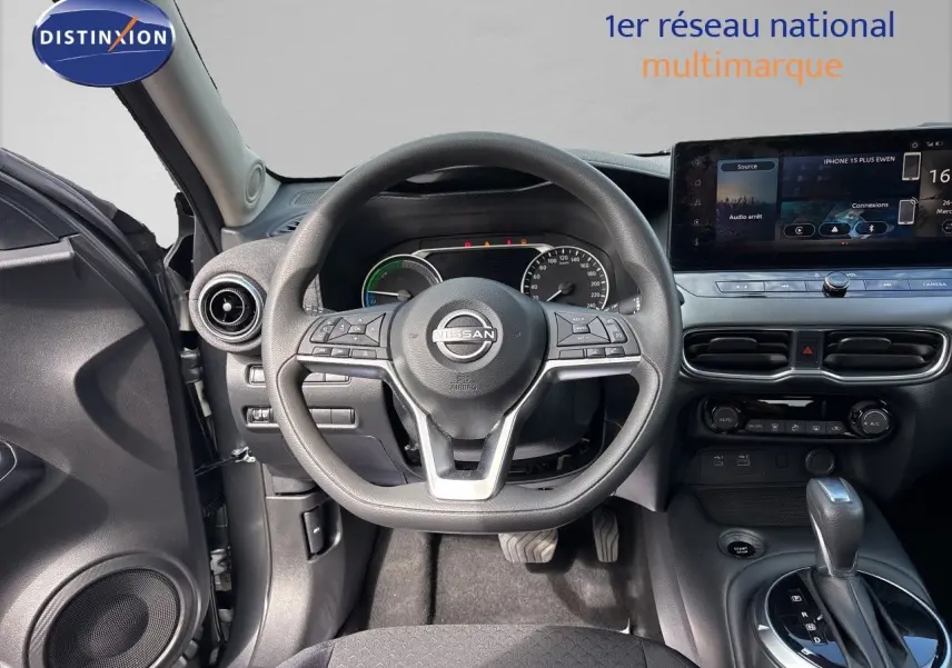 Vue intérieure centrée sur le volant et le tableau de bord du Nissan Juke Hybrid gris, avec écran tactile et levier de vitesse automatique.