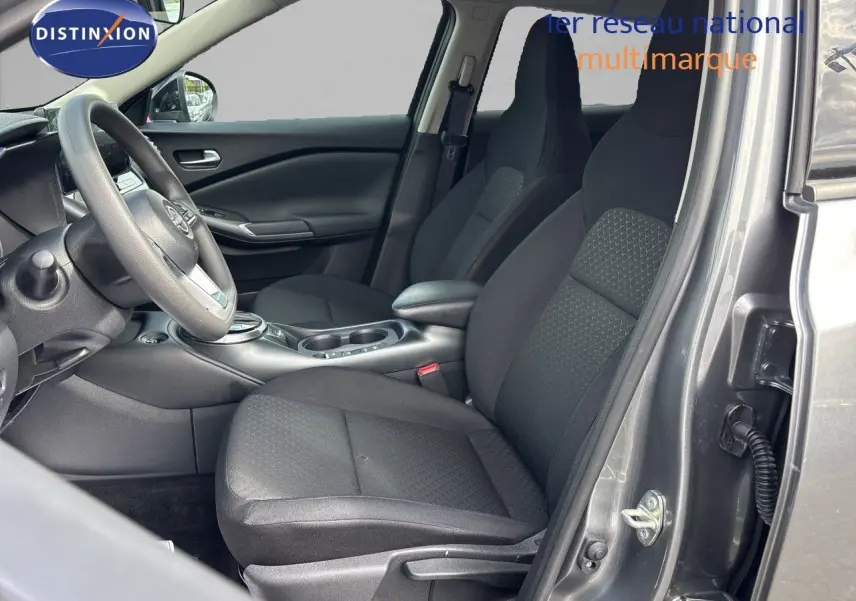Vue intérieure côté conducteur du Nissan Juke Hybrid 2024 en gris squale métal, sièges tissu noir et volant multifonction.