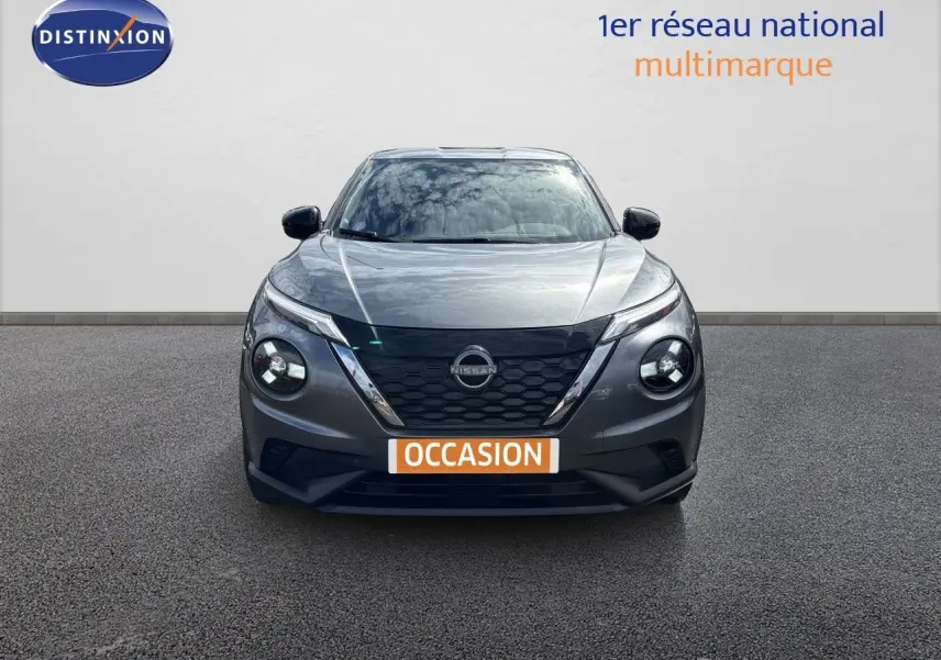 Vue frontale d'un Nissan Juke Hybrid 143ch Business Edition gris squale métal avec calandre noire et phares ronds allumés.
