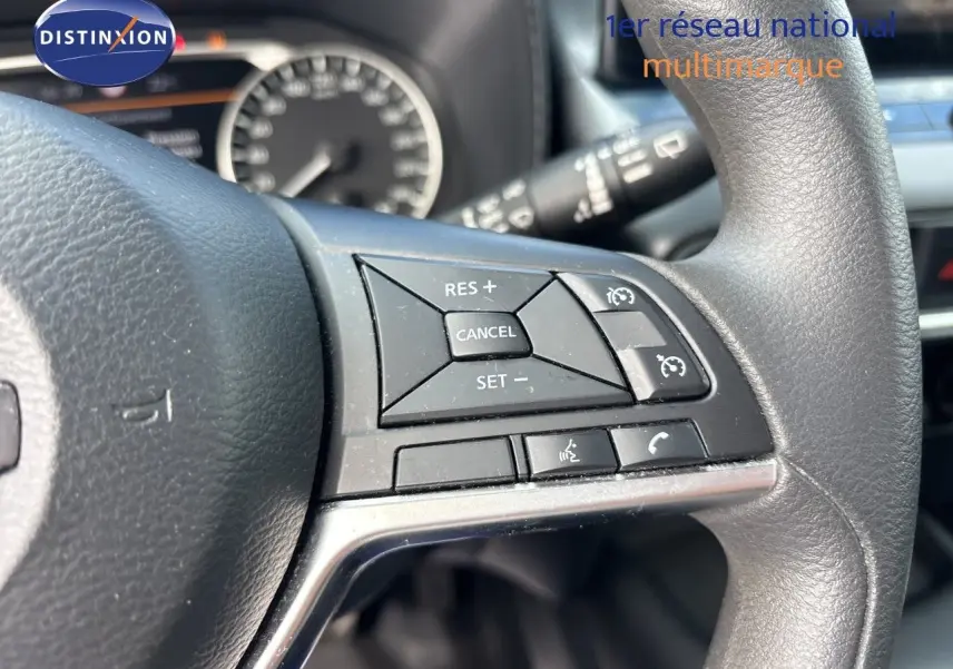 Gros plan sur les commandes au volant du Nissan Juke Hybrid 2024, avec tableau de bord flou en arrière-plan.
