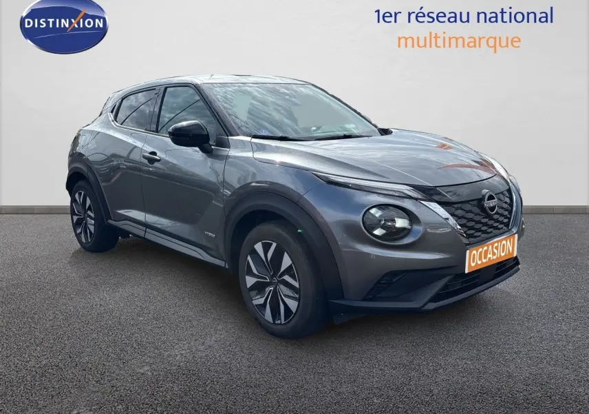 Nissan Juke Hybrid gris squale metal en 3/4 avant droit, avec jantes stylisées et calandre noire distinctive.