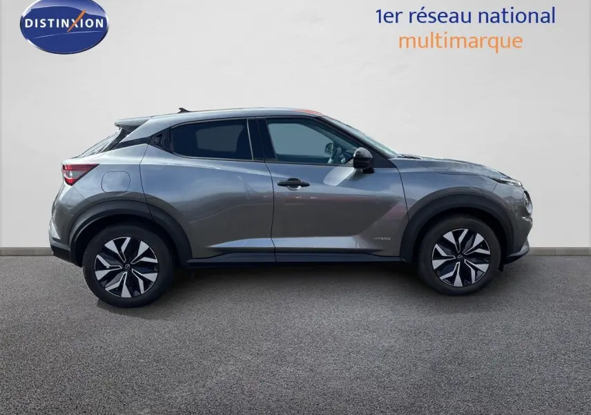 Profil latéral droit du Nissan Juke Hybrid 143ch Business Edition gris squale métal avec jantes noires et détails hybrides visibles.