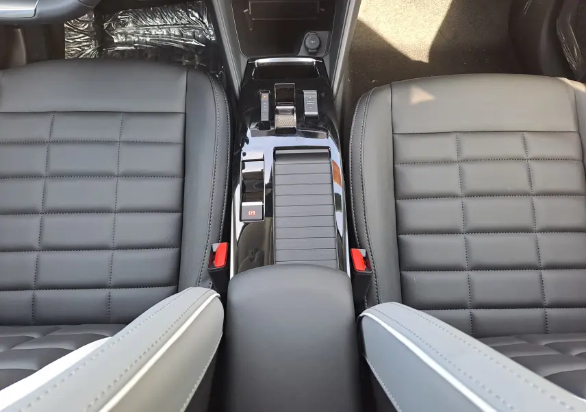 Vue plongeante sur la console centrale noire brillante et les sièges gris anthracite en cuir et tissu du Citroën C4 hybride 2025.