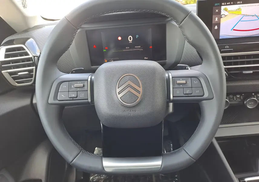 Vue rapprochée du volant noir de la Citroën C4 hybride 2025, avec commandes intégrées et tableau de bord numérique.