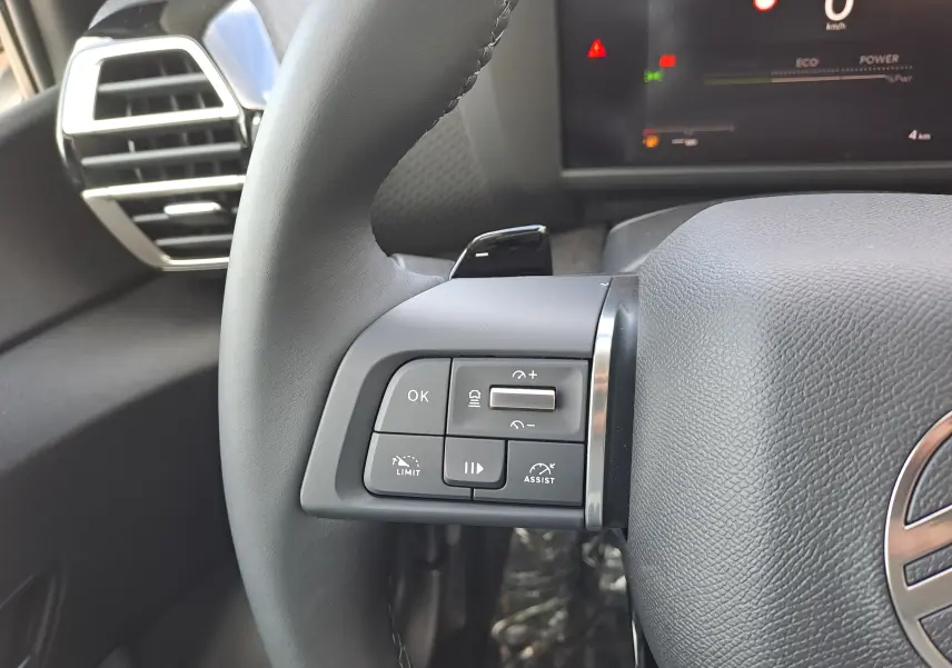 Gros plan sur les commandes au volant à gauche du Citroën C4 hybride 2025, intérieur gris noir moderne.