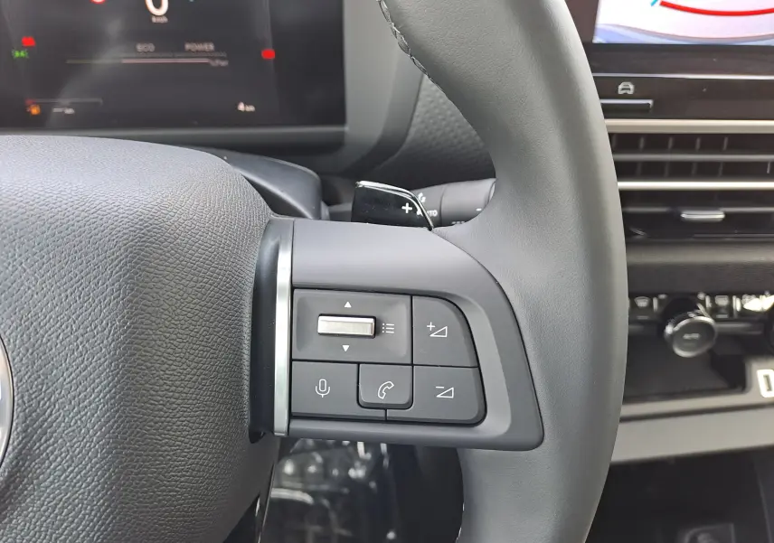 Gros plan sur le côté gauche du volant gris noir du Citroën C4 hybride 2025, avec commandes audio et téléphone intégrées.