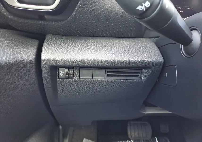Détail du tableau de bord noir côté gauche avec commande de réglage des phares sur Citroën C4 hybride 2025.