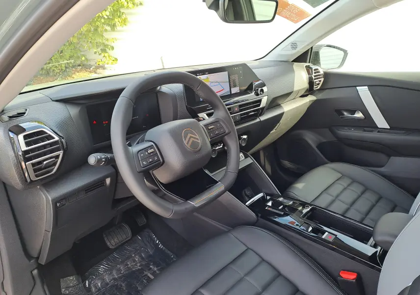 Vue intérieure côté conducteur de la Citroën C4 hybride 2025 avec tableau de bord noir et volant multifonction.